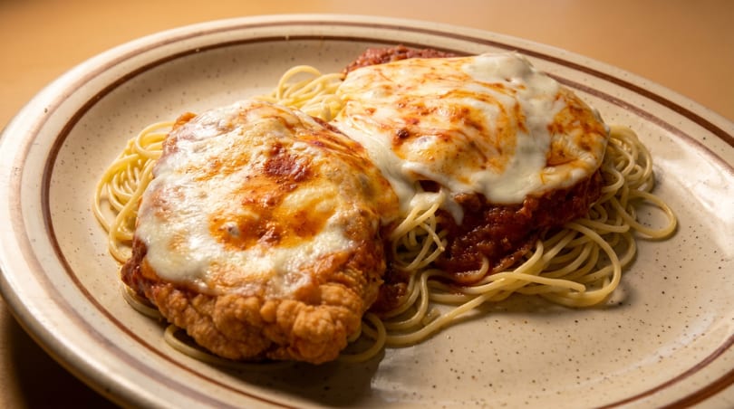 Two chicken parmesan cutlets with melted cheese and marinara sauce on a bed of spaghetti.
